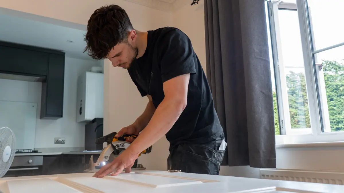Trimming a white panel door with a circular saw after new flooring in Warwickshire